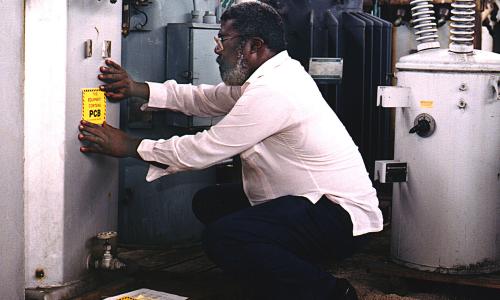 A person kneeling down and labeling equipment that contains PCBs.