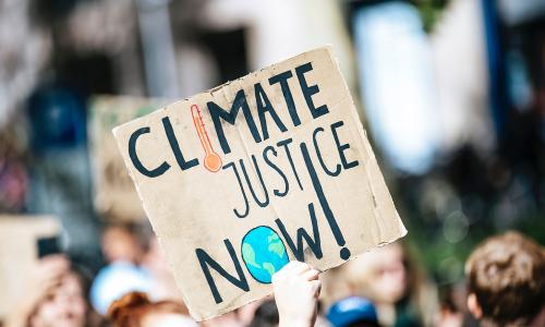 Activist holding up a climate justice now sign