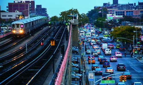 Cars sit in traffic while a train passes them by. 